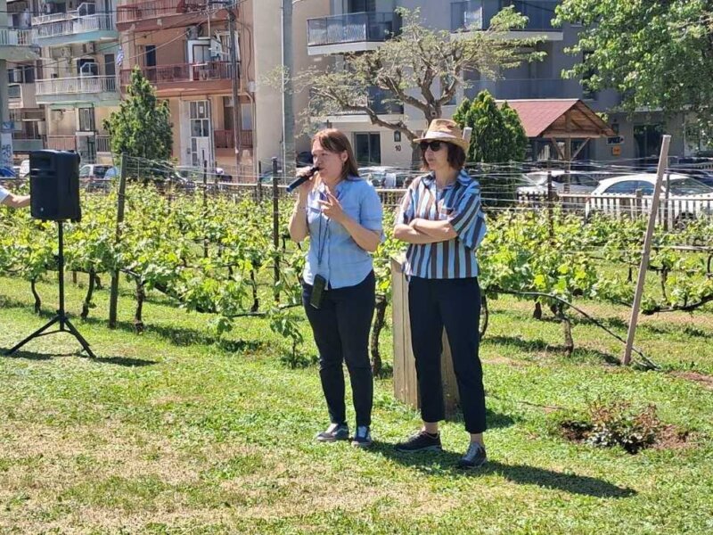 Two women speaking to an audience in an urban vineyard